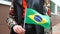 Unrecognizable woman holding Brazilian flag. Girl walking down street with national flag of Brazil