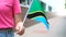 Unrecognizable woman holding Tanzanian flag. Girl walking down street with national flag of Tanzania