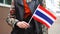 Unrecognizable woman holding Thai flag. Girl walking down street with national flag of Thailand