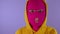 Unrecognizable woman in pink balaclava smiles on purple background. Unknown female in mask smiling and looking at camera