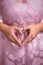 Unrecognizable woman in pink puffy dress makes with her hands a heart sign of love. Pink manicure. Medium close up shot