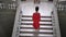 Unrecognizable woman in red dress on high heels climbs a large staircase