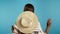 Unrecognizable woman with straw hat dancing with her back to camera on blue background. Trendy girl. Party, happiness