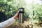 Unrecognizable woman traveler holding thermos mug on background of green forest. Travel, hiking, sport, healthy lifestyle concept