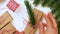 Unrecognizable woman wrapping gift box with brown kraft paper, using red white rope to tie bow-knot inserting pine twig.