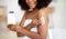 Unrecognizable young black woman applying lotion on her body, pampering skin afterbath or shower at home, closeup