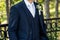 Unrecognizable young groom in elegant dark blue suit with beautiful white roses boutonniere. Groom fashion detail shot.