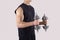 Unrecognizable young sportsman working out with dumbbells over light studio background, closeup