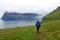 Unrecognizable young woman hiking down a grassy hill and towards the ocean.