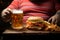 Unrecognized figure grips beer and hamburger, representing undisclosed indulgence and anonymity