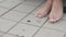 Unrecognized girl`s bare feet in a long dress walking on city tiles.