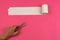 Unrolled roll of rough recycled white toilet paper on pink background and human hand with scissors, close-up, copy space