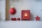 Unsharp red christmas ball at a branch in front of a shelf with red christmas decoration, star, lantern with candle light