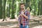 Unshaven handsome man in open plaid shirt with jeans carry large splitting axe in summer forest natural landscape