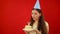 Unsuccessful attempt to blow out the candle and make a birthday wish. Young woman in a festive cap holds a plate with a slice