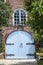 Unusual blue wooden arched garage door with big ornate hinges in brick house with small balcony with table and chairs directly