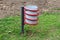 Unusual funky twisted public trash can with decorative red spiral surrounding grey metal can mounted on dark metal pole