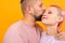 Unusual pretty woman with short pink hair and tattoo enjoys life with her boyfriend isolated on orange background