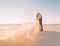 Unusual wedding in the desert. A girl in a white dress ivory shade. Very long plume fluttering in the wind. A loving