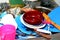 Unwashed kitchen utensils in the wash basin need to be cleaned and washed, a pile of dirty dishes, knives, pots and drinking glass