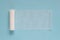 Unwound roll of white sterile medical bandage for dressing wounds on a blue background, copy space