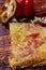 Up-close half pizza slice with ham, salami and cheese on wooden background with fresh ingredients on top