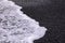 Up close photo of a white foam after a big wave running on the black sand
