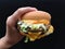 Up close a special beef burger in hand over black background with selective focus.