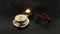 Ð¡up of coffee. Feminine black and red eyeglasses. Black dark background. Sauser with flowers and love hearts. Burning candle.