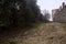 Uphill dirt path bordered by an olive tree grove and an ancient boundary wall on a cloudy day