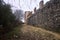 Uphill dirt path bordered by an olive tree grove and an ancient boundary wall on a cloudy day