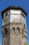 The upper part of an ancient watchtower made of stone blocks and wood paneling with windows against the blue sky on a bright sunny