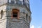 The upper part of an ancient watchtower made of stone blocks and wood paneling with windows against the blue sky on a bright sunny