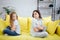 Upset and angry girls sit on yellow sofa and look at eah other. They hold hands crossed. Teenagers have a quarrel