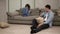 Upset angry young caucasian girl feeling offended by boyfriend or husband while he is sitting on the floor. Woman