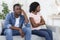 Upset black man and woman sitting on couch at home