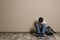 Upset boy with backpack sitting on floor at color wall. Space