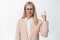 Upset businesswoman in glasses pointing finger up, frowning displeased, showing smth bad on top, white background
