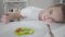 Upset Caucasian girl with fork lying on table and looking at salad of sliced tomato and cucumber. Young unhappy woman