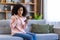 Upset disappointed woman at home received online message message with bad news, depressed hispanic woman sitting on sofa