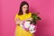 Upset disappointed young woman standing with folded arms, holding flowers in one hand, looking aside, having unpleasant facial