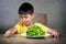 Upset and disgusted hispanic kid sitting on table in front of spinach plate unhappy rejecting the fresh food finding it disgusting