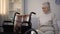 Upset elderly woman sitting on sofa near wheelchair in rehabilitation center