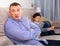 Upset father sitting after quarrel at home, son on background