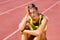 Upset female athlete sitting on running track