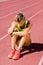 Upset female athlete sitting on running track