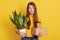 Upset female dresses casual clothing holding her staff and flowerpot with bowstring hemp in hands, looking at camera with sad look