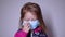 Upset little blonde girl in a blue medical mask. takes off the mask. in a pink sweater. covid 19 pandemia. kids on