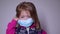 Upset little blonde girl in a blue medical mask. takes off the mask. in a pink sweater. covid 19 pandemia. kids on