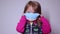 Upset little blonde girl with a blue medical mask. trying to put it on. in a pink sweater. covid 19 pandemia. kids on